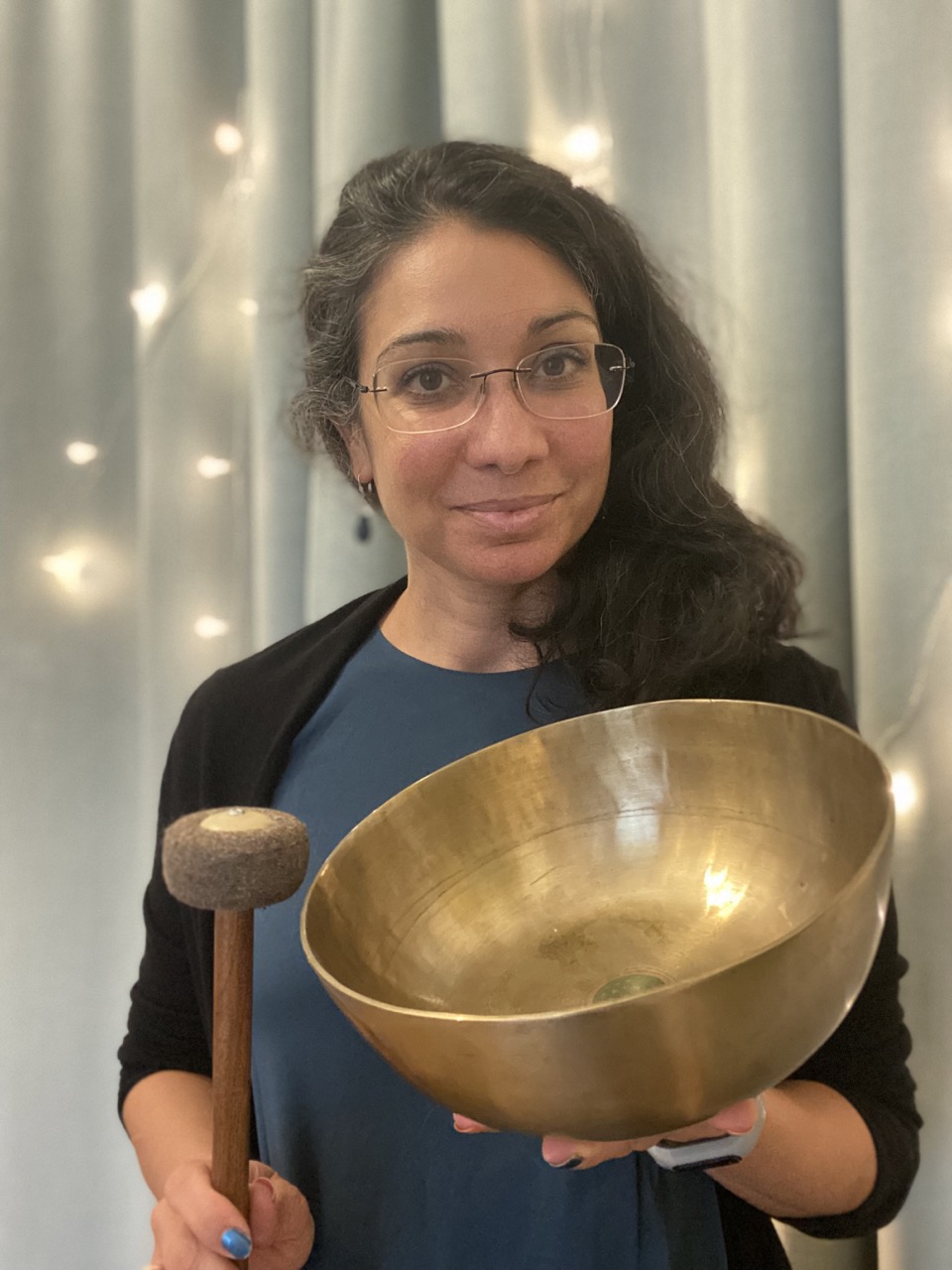 Rani Gindl hält eine große Klangschale in den Händen und lächelt in die Kamera. Im Hintergrund sanfte Lichter – eine ruhige, einladende Atmosphäre für Klangmassage.